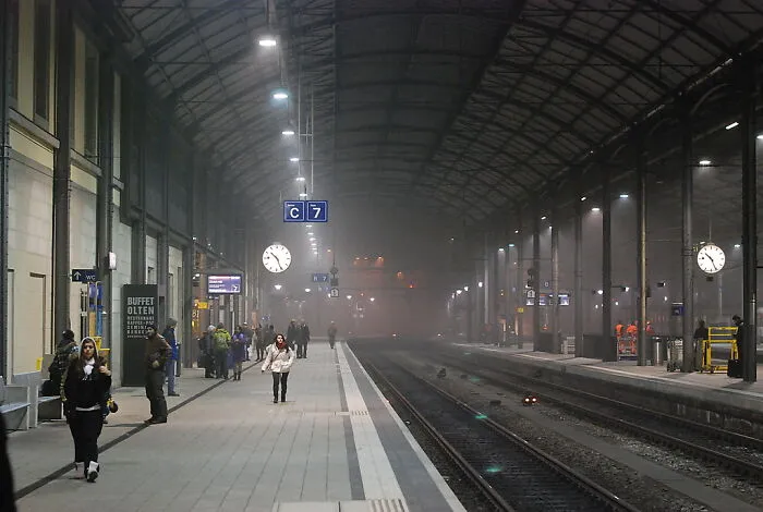 People walking on a misty train station platform under large arched roof at night, capturing local inside jokes atmosphere.