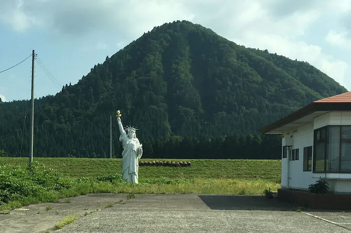 Small Statue of Liberty replica in a rural field with mountain backdrop, an impressive thing countries implemented.