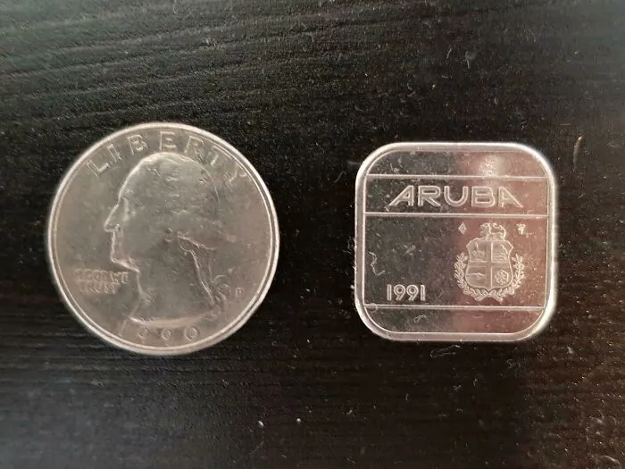 Small square Aruba coin from 1991 displayed next to a US quarter, showcasing an impressive unique currency design.