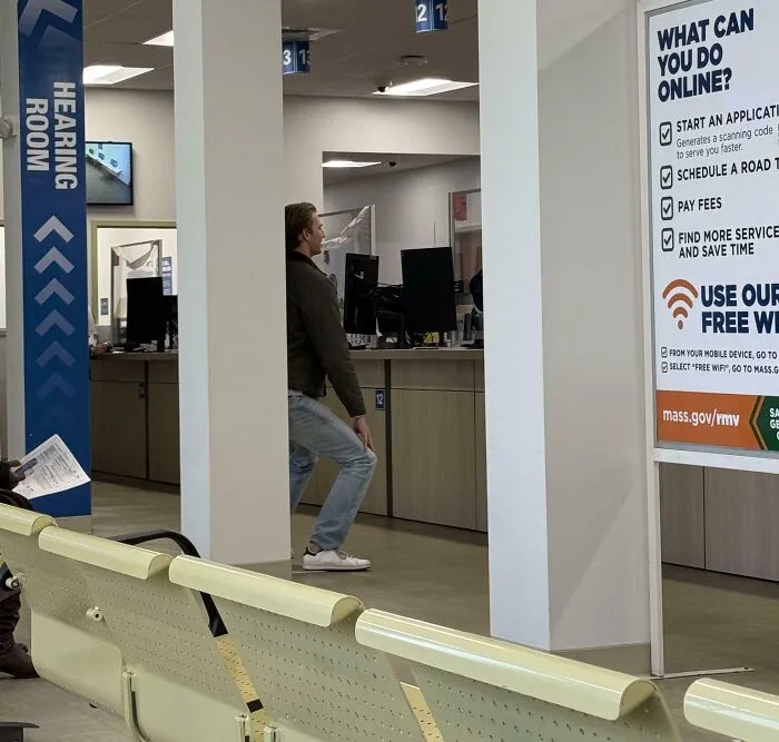 Tall person ducking to avoid hitting head on a low ceiling beam inside a public office waiting area.