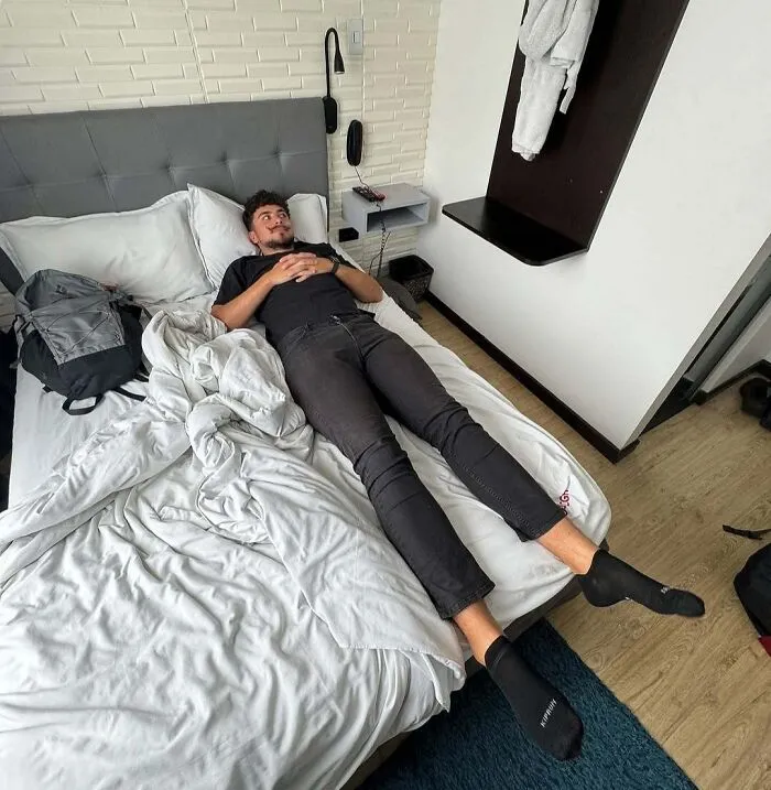 Tall man lying on a small bed illustrating common struggles only tall people face in daily life.