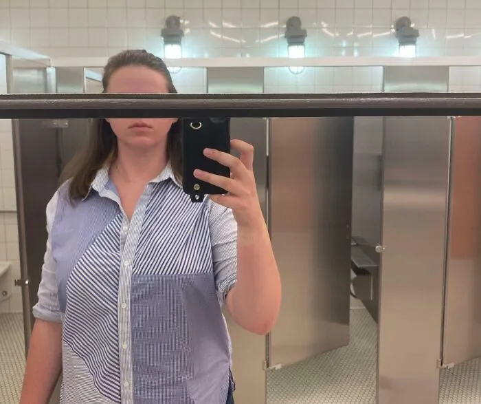 Tall person taking a mirror selfie in a public restroom, illustrating struggles only tall people face with limited mirror height.