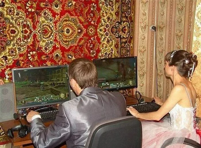 Bride and groom playing video games on dual monitors in wedding attire, an awkward wedding photo moment.