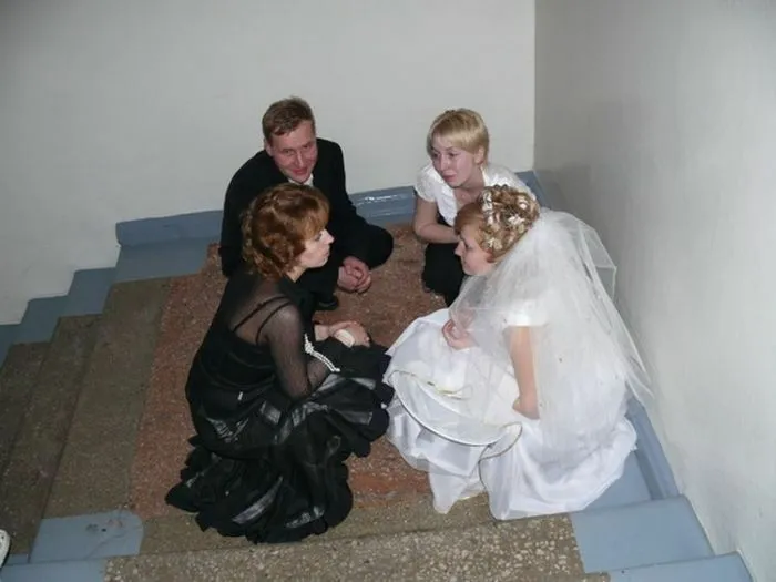 Four people including a bride in a wedding dress sitting awkwardly on stairs in an awkward wedding photo moment.