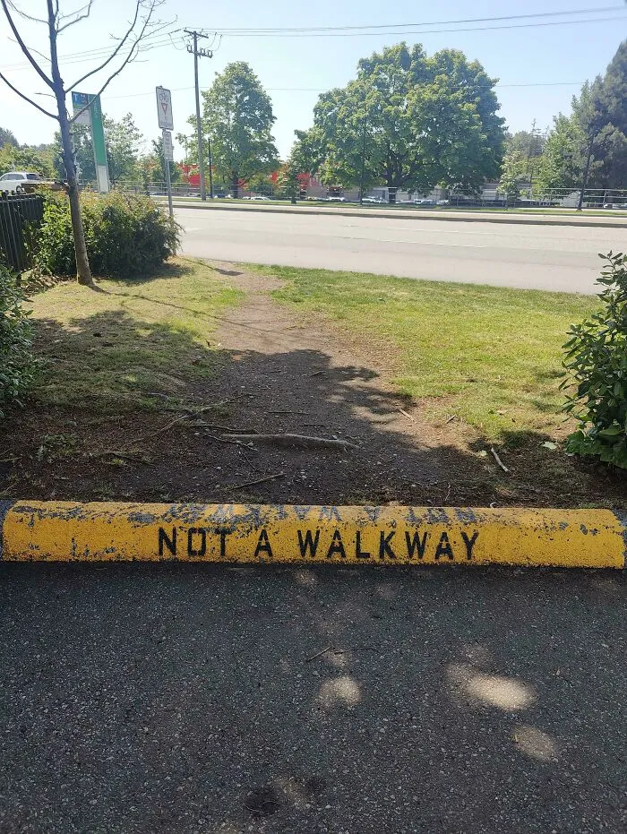 Desire path worn through grass showing how people walk despite city planning and signage restricting access.