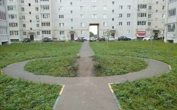 Grass desire paths cutting through paved city walkways in an urban residential area showing practical pedestrian routes.