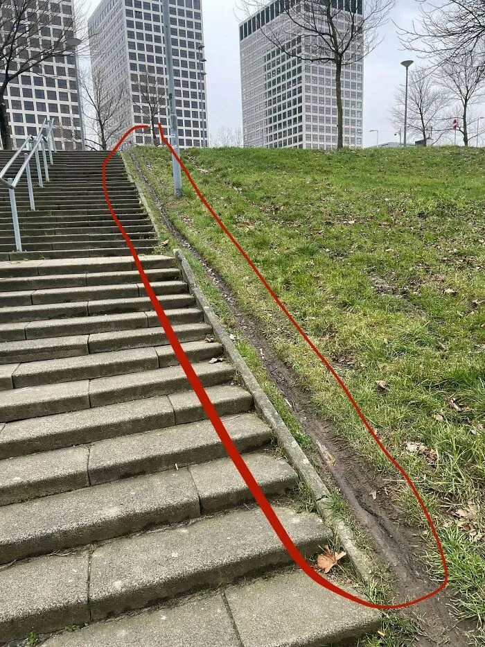 Desire path worn on grassy slope beside city stairs showing how people walk versus planned routes in urban areas.