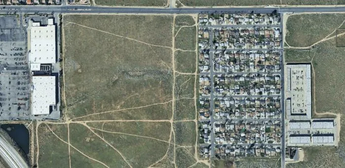 Aerial view of desire paths cutting across open land beside a residential neighborhood, illustrating city planning vs real walking routes.