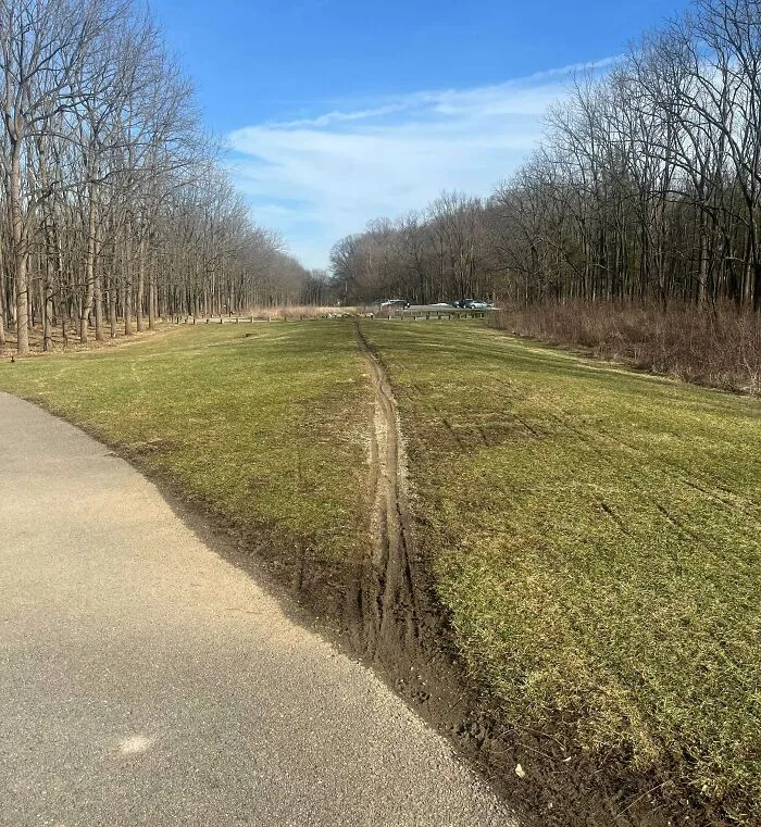 Desire path worn through grass beside paved trail, showing how people walk differently from planned city paths.