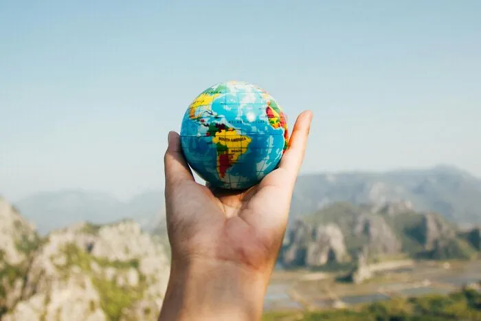 Hand holding a small globe outdoors with a mountain landscape, symbolizing global perspective on worst coworkers.