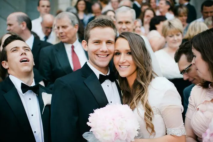 Bride and groom smiling at wedding while awkward guest makes a funny face in a group wedding photo.