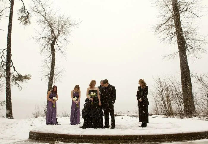 Bride and groom stand with bridesmaids in snowy outdoor setting, creating awkward wedding photo moment.