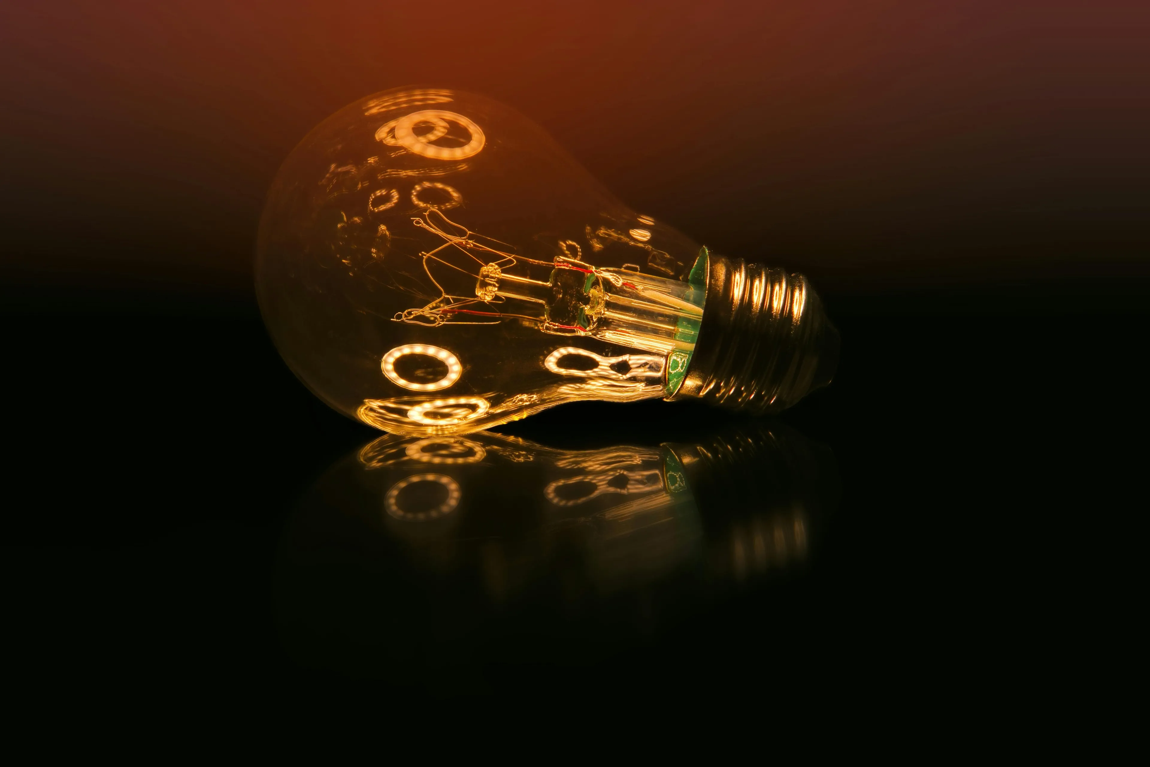 Glossy antique light bulb glowing softly and reflecting on black surface, representing deadly decoys of past inventions.