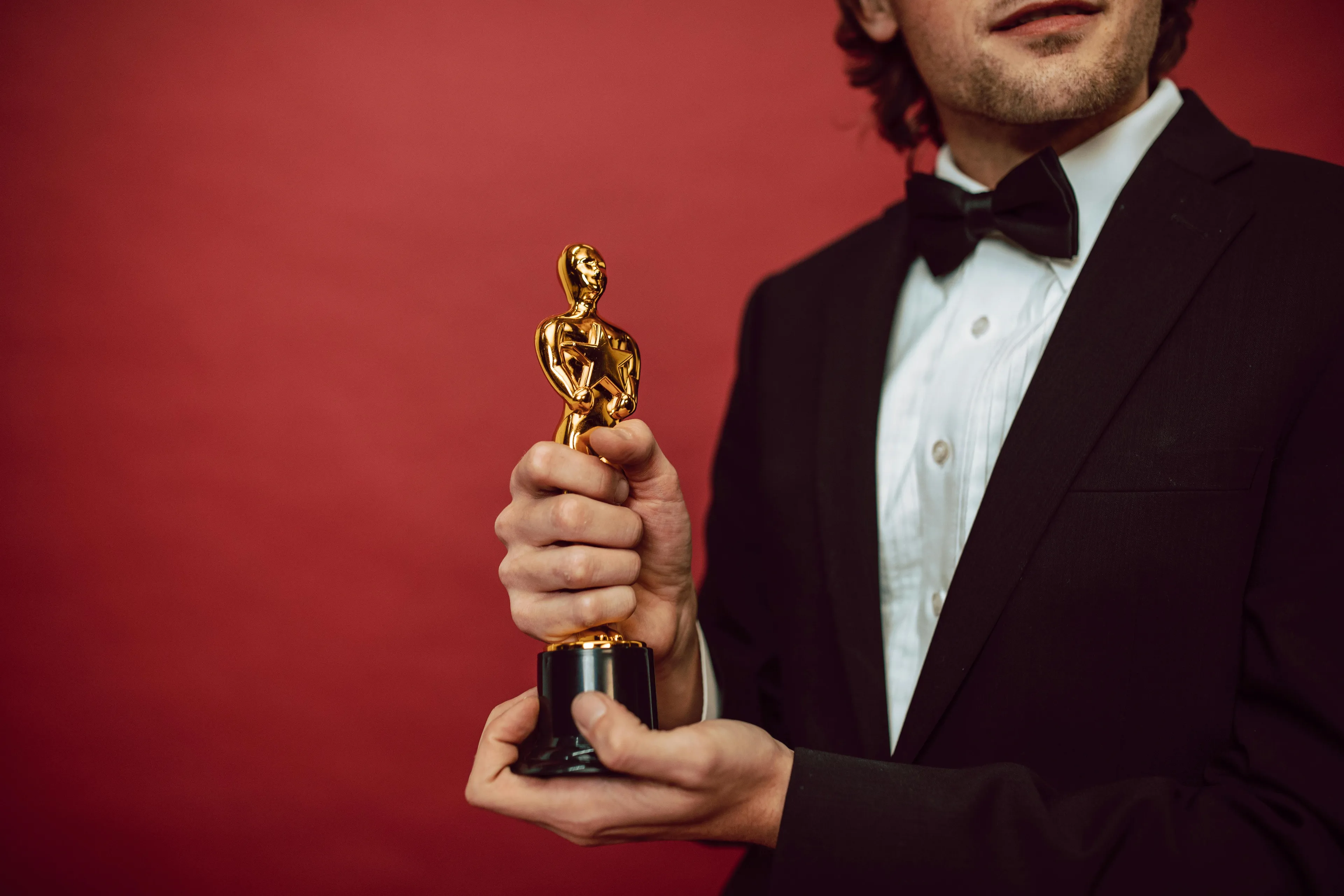 Man in tuxedo holding a golden Academy Award statuette against a red background for deadly decoys quiz.