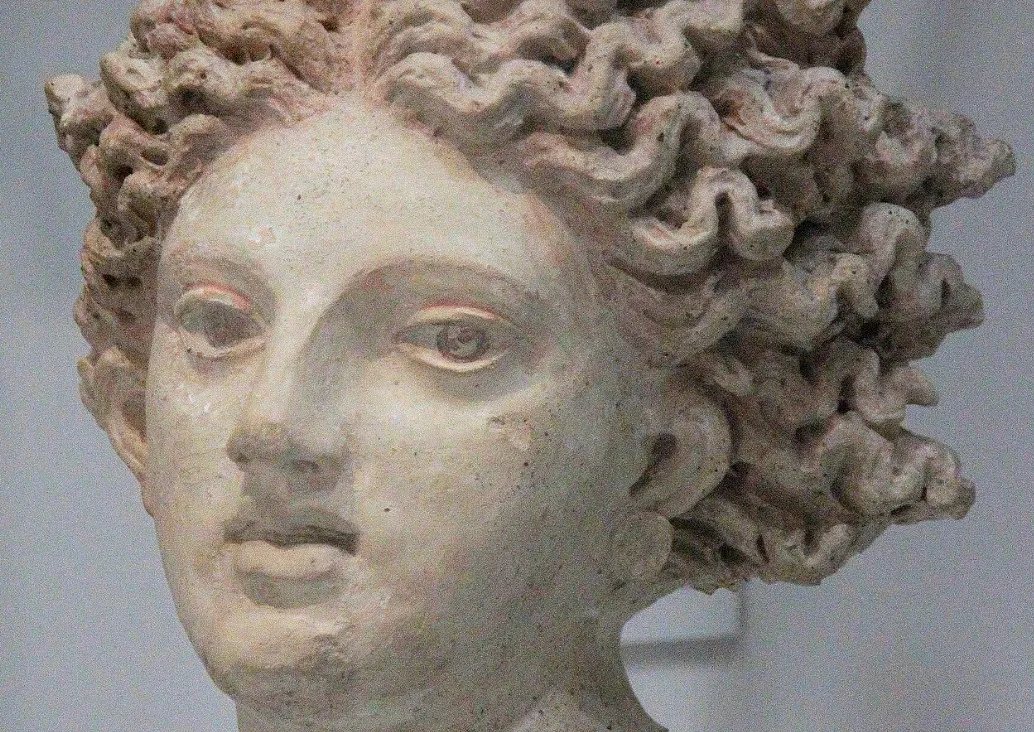 Close-up of an ancient Greek statue head featuring detailed curly hair, representing a deadly decoy Greek god or goddess.