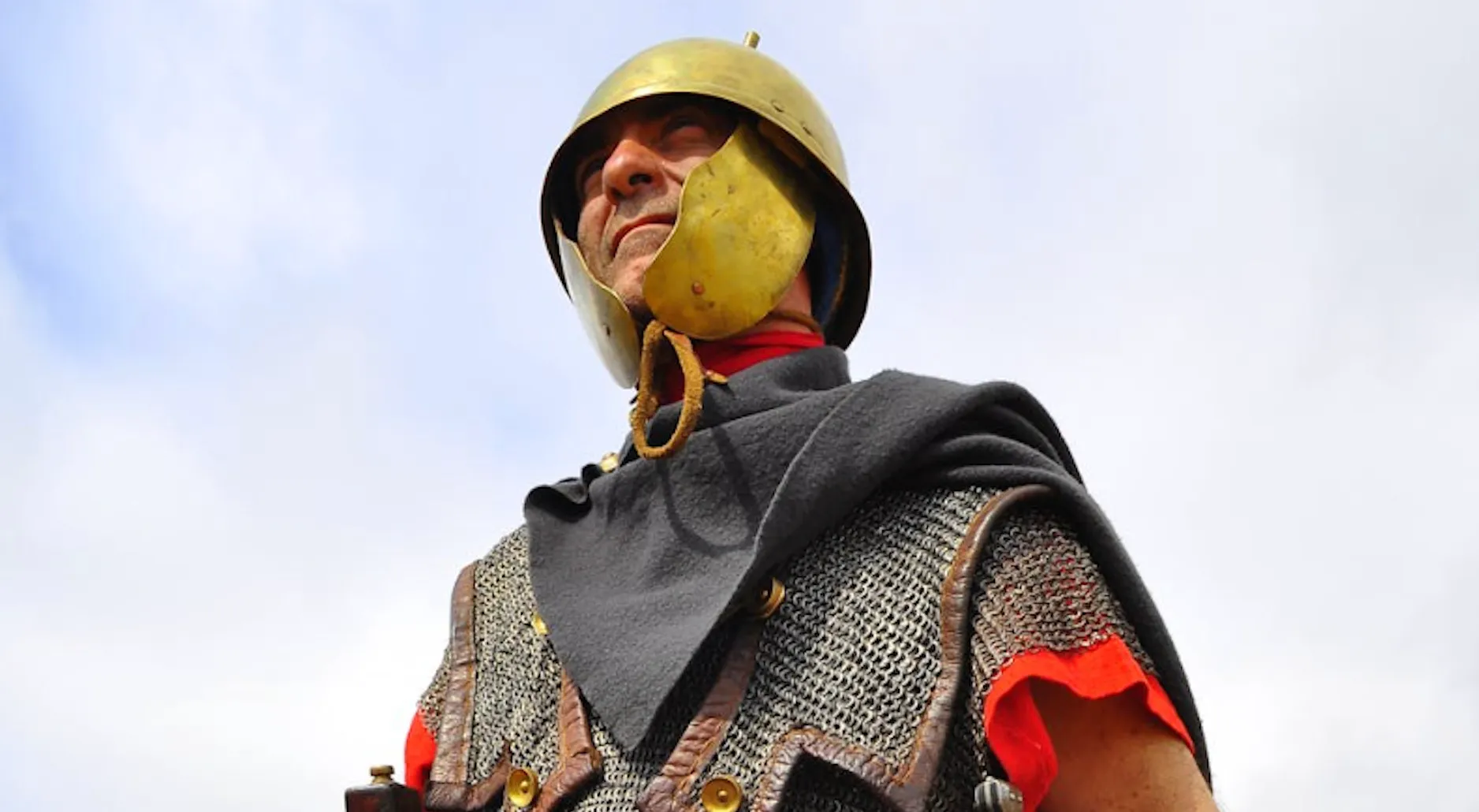 Roman soldier in historical armor and helmet looking upwards with sky background in deadly decoys context