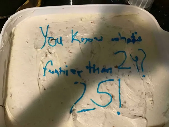 Dessert with uneven icing and messy writing in blue icing, showing a failed attempt to decorate a cake.
