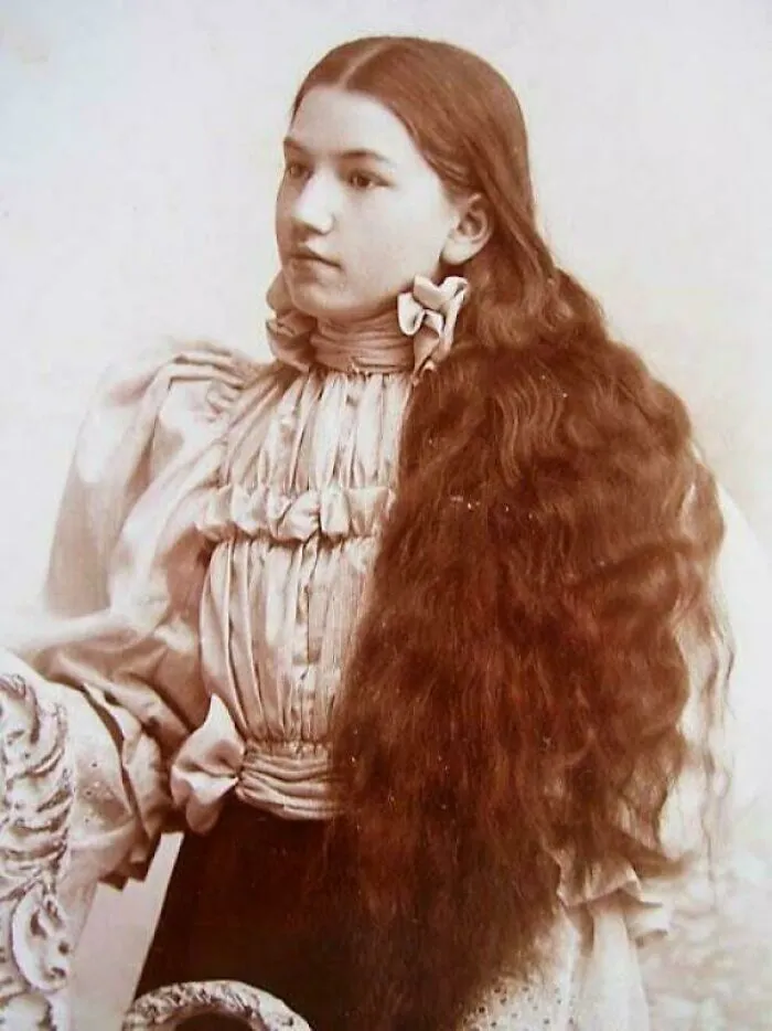 Young woman from the Victorian era wearing a high-necked blouse with long, thick hair styled with a bow, vintage portrait.