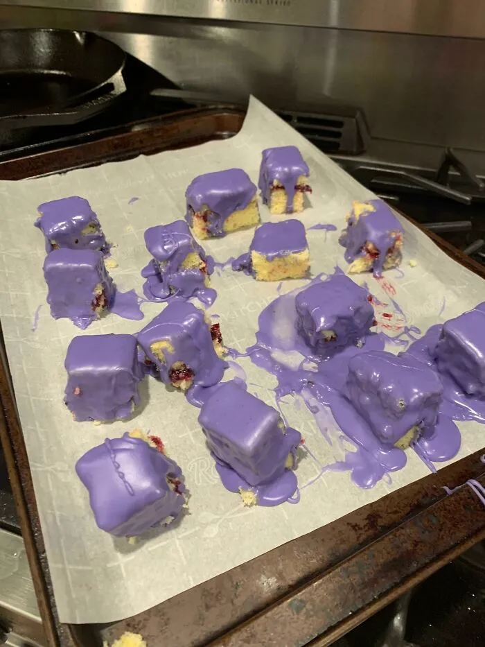 Chunks of dessert on parchment paper with uneven purple icing melted and dripping, showing a ruined dessert attempt.
