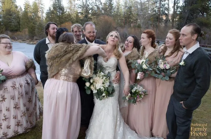 Group of wedding guests and bridal party awkwardly posing outside with bride in white dress holding bouquet in awkward wedding photo