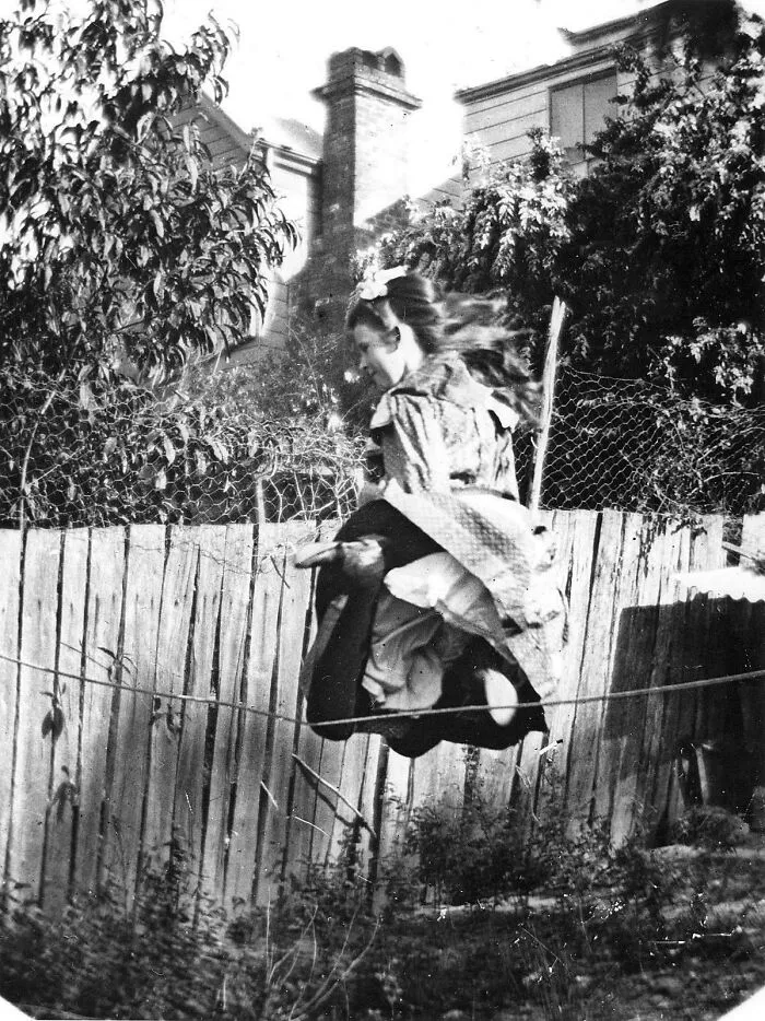 Young Victorian girl jumping over a fence with a broomstick, capturing a playful moment from the Victorian era.