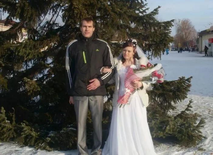 Bride in white wedding dress holding flowers with groom in casual jacket posing outside near a tree awkward wedding photo
