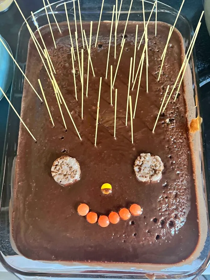 Baking disaster with a burnt chocolate dessert decorated awkwardly with cookies, candy, and uncooked spaghetti sticks.