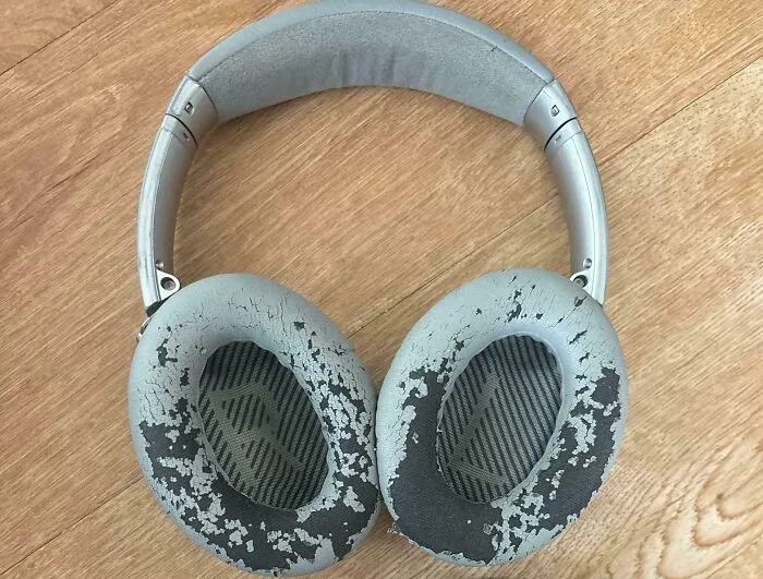 Worn down headphones with cracked and peeling ear cushions showing signs of everyday object wear.