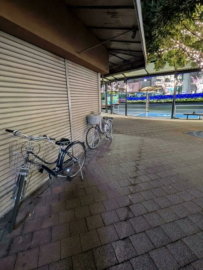 Bicycles leaning against a worn, scratched metal shutter in an urban area at night showing unexpected wear.