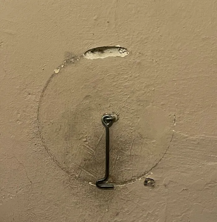 Worn down wall area showing circular marks and a bent metal hook, illustrating everyday objects wearing down unexpectedly.
