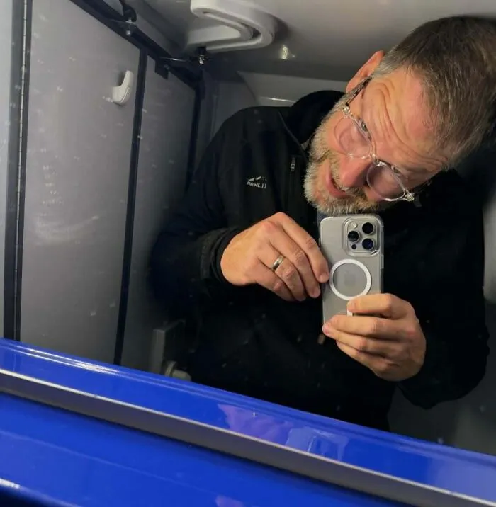 Man wearing glasses and black jacket struggling to fit inside a small space, illustrating common struggles tall people face.