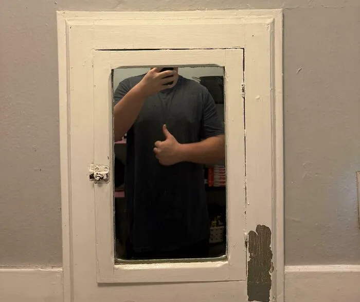 Person with a tall stature giving a thumbs up in a small mirror, highlighting struggles only tall people face.