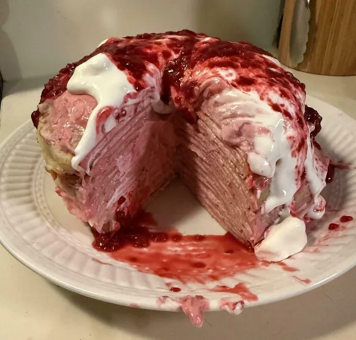 Messed up dessert with smashed layers and uneven topping of cream and berry sauce spilling over the plate.