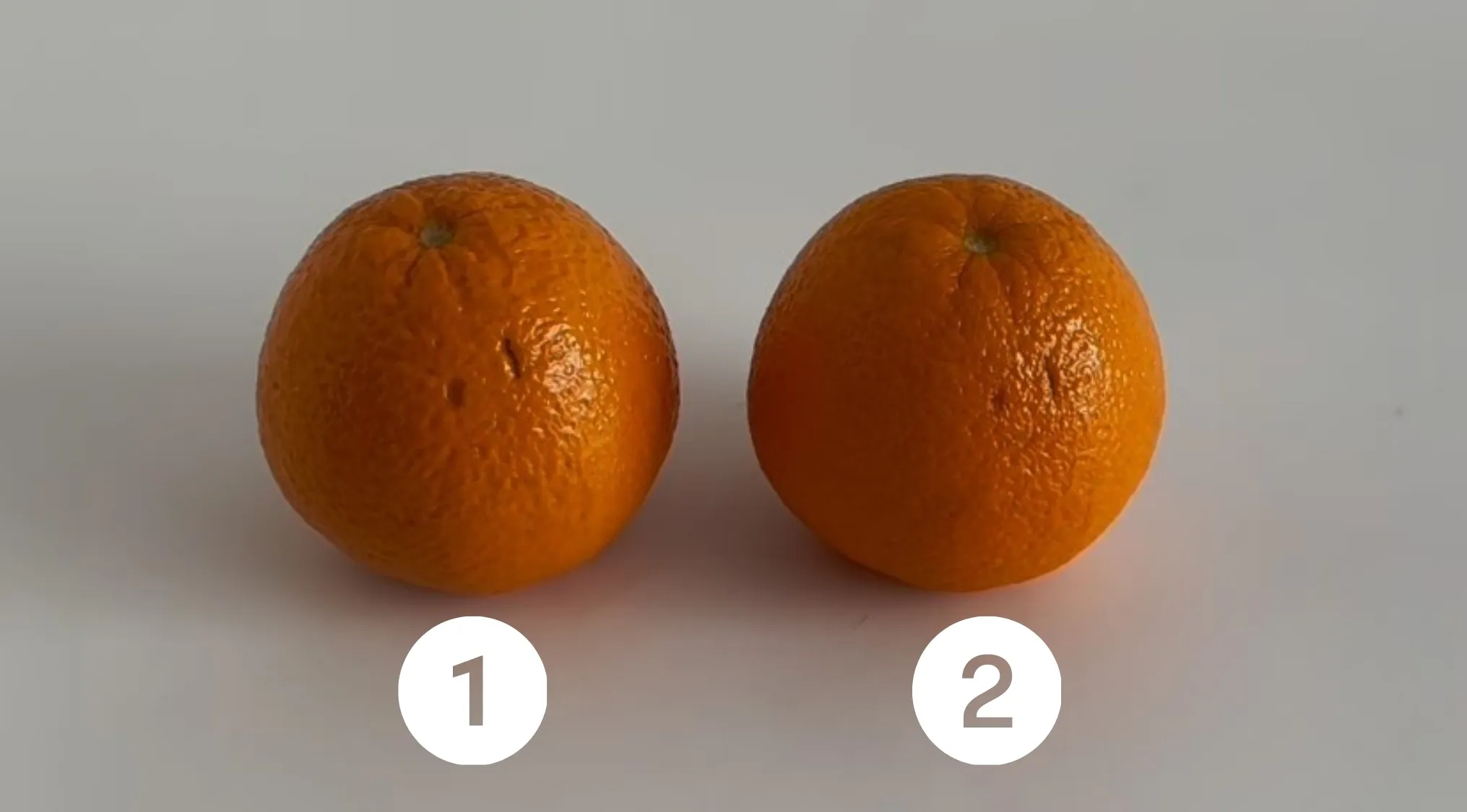 Two oranges labeled 1 and 2 on a white surface in a real or cake visual challenge.