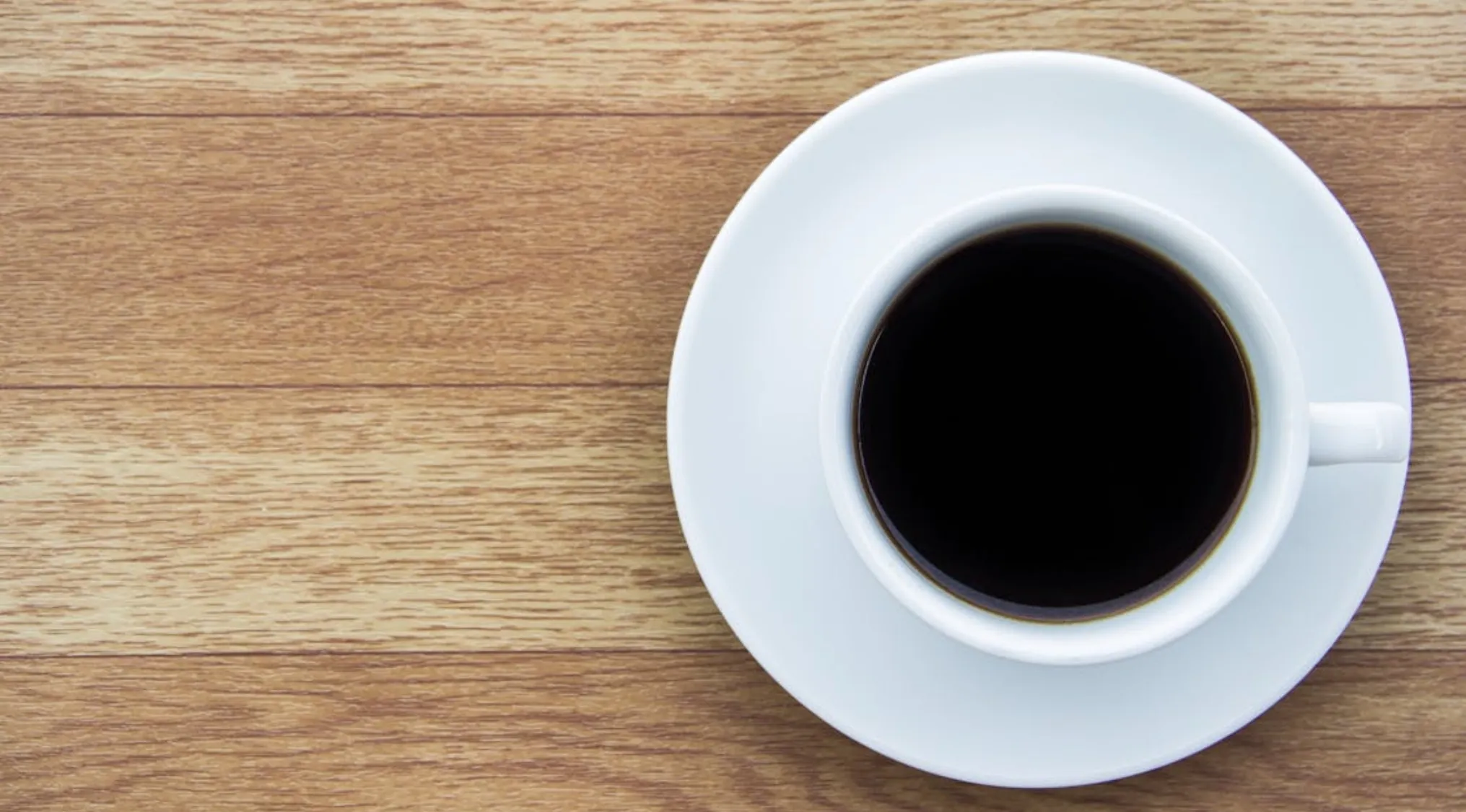 White cup filled with black coffee on a wooden surface, prompting the question is it real or cake.