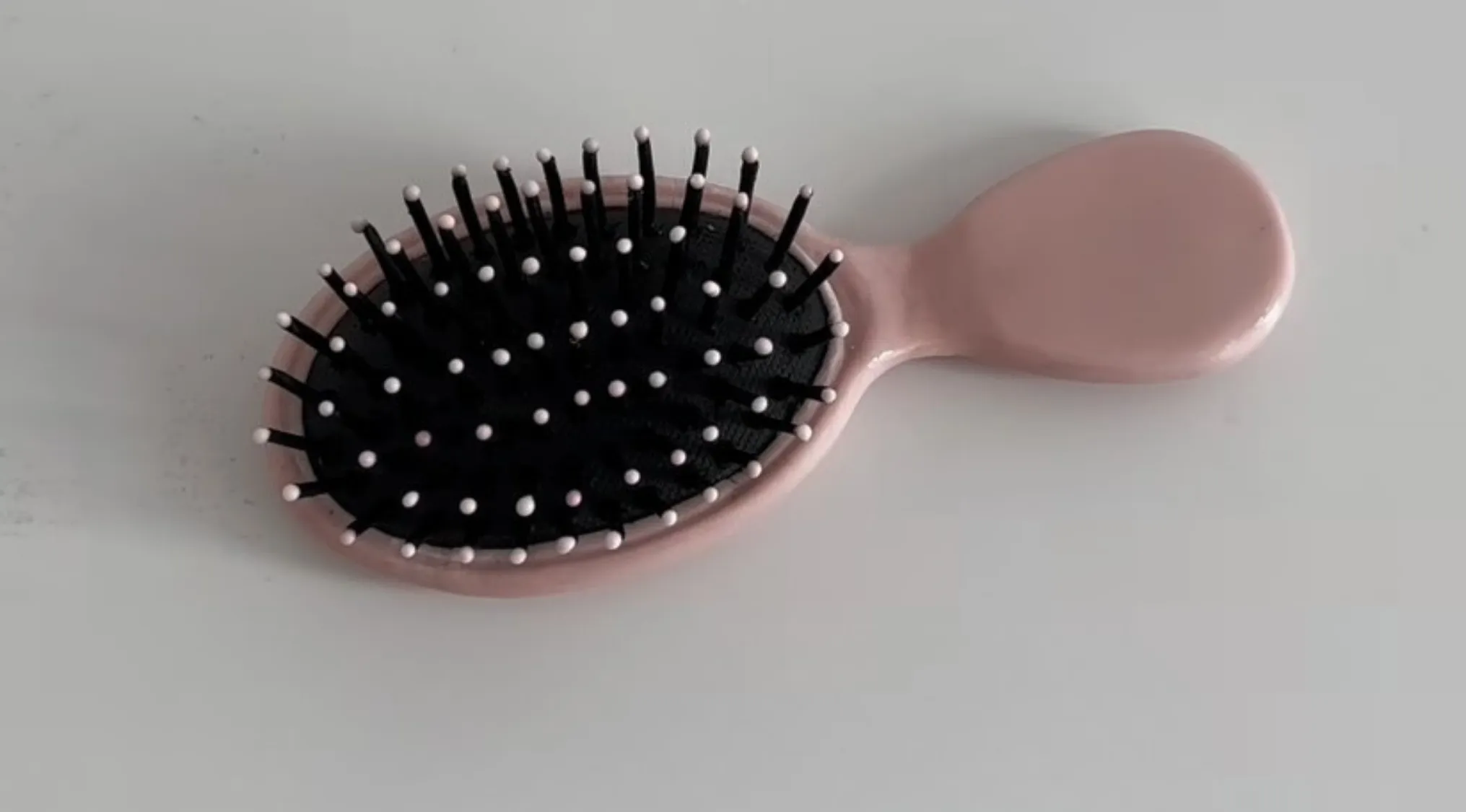 Pink hairbrush edible illusion cake with realistic black bristles on a light gray surface showing real or cake detail.