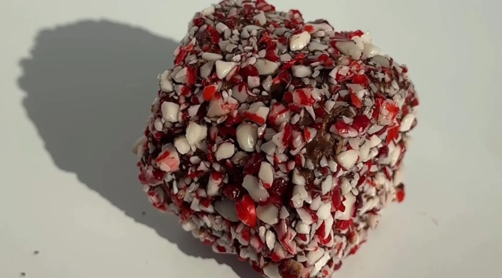 Close-up of real candy pieces covered with crushed red and white peppermint bits on a plain surface, exploring texture details.