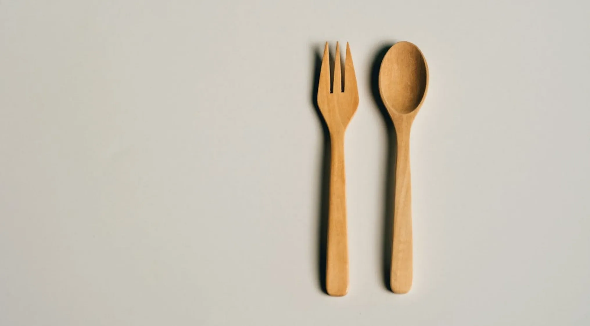 Wooden utensils including a fork and spoon placed on a plain surface, showcasing real wooden texture and design.