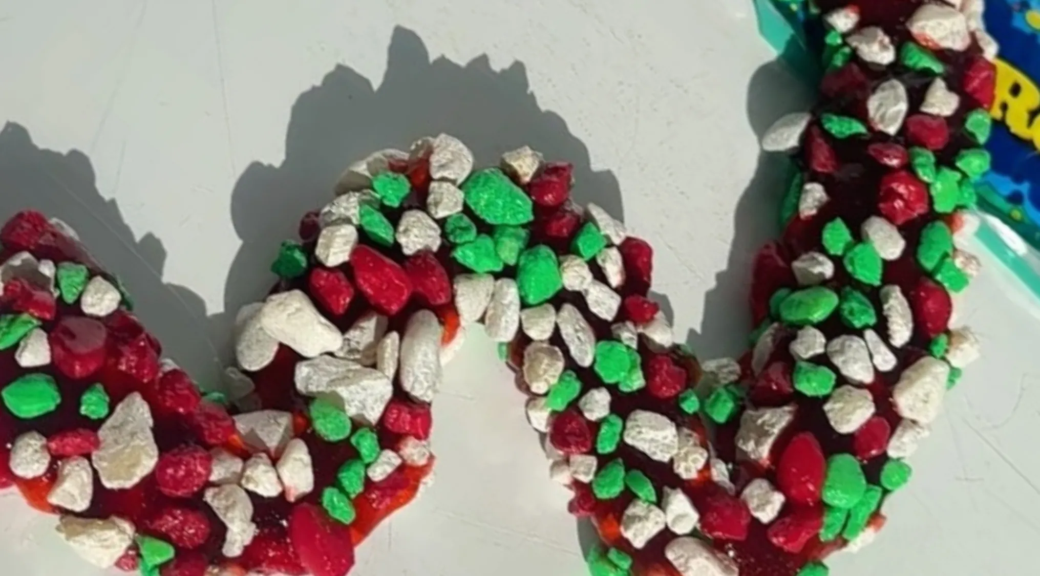Close-up of a red, green, and white gummy or slime candy with a textured surface resembling crushed candy pieces.