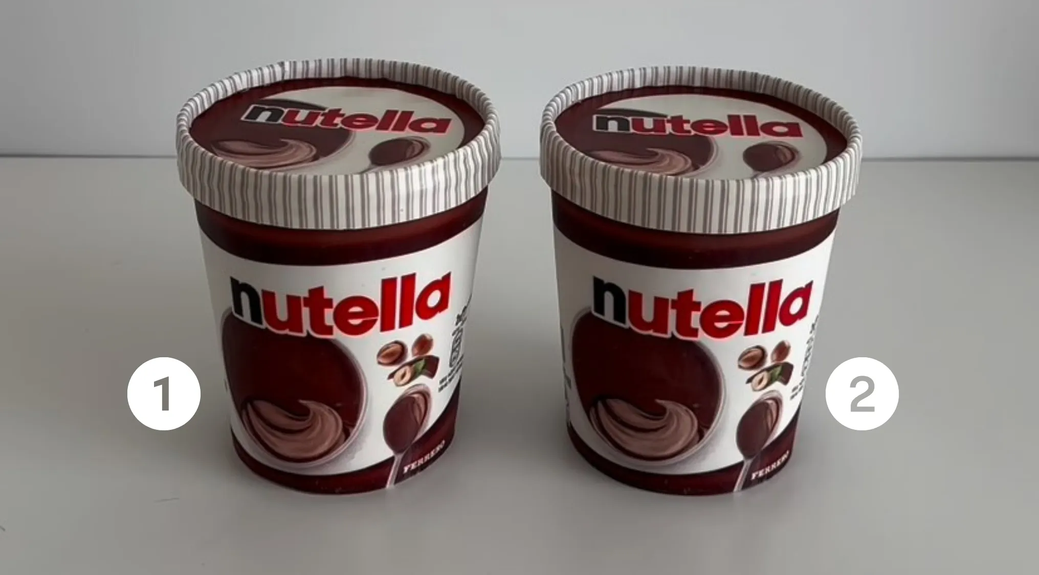Two Nutella containers side by side on a table, labeled 1 and 2, challenging viewers to spot which one is real cake.