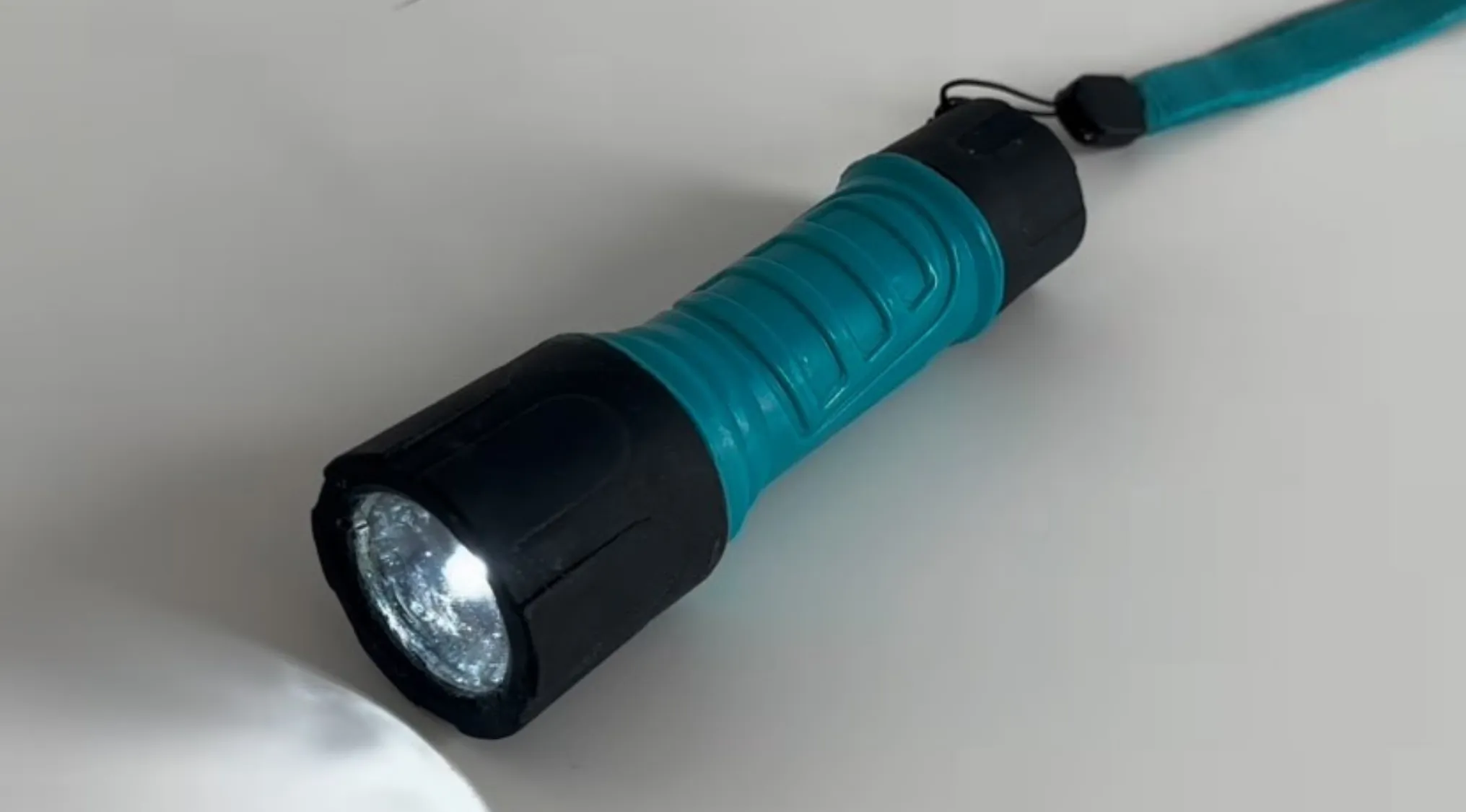 Blue and black flashlight turned on, placed on a white surface, illustrating the real flashlight or cake question.