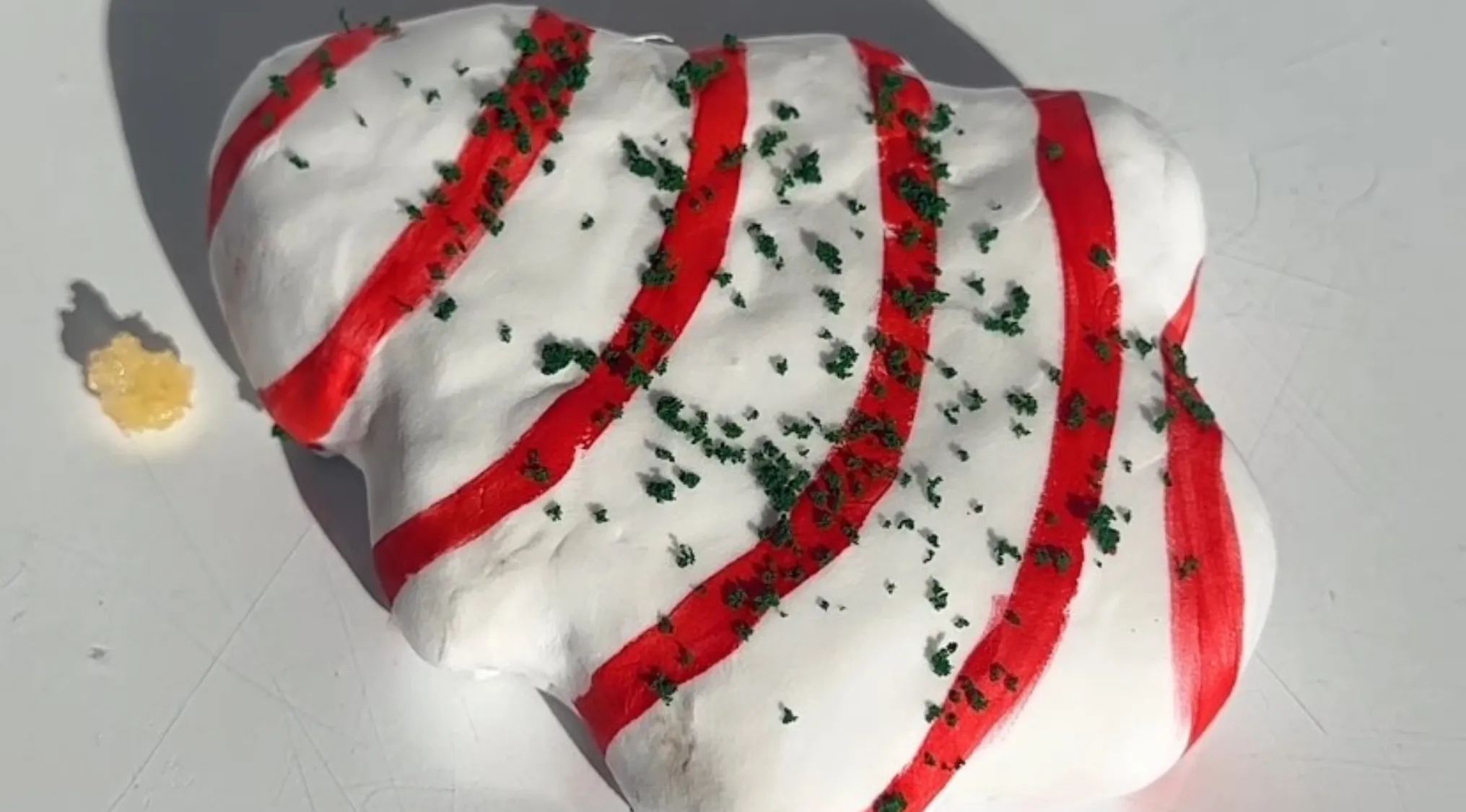 White slime with red stripes and green specks resembling cake decoration on a light surface, a bit tricky to tell which.