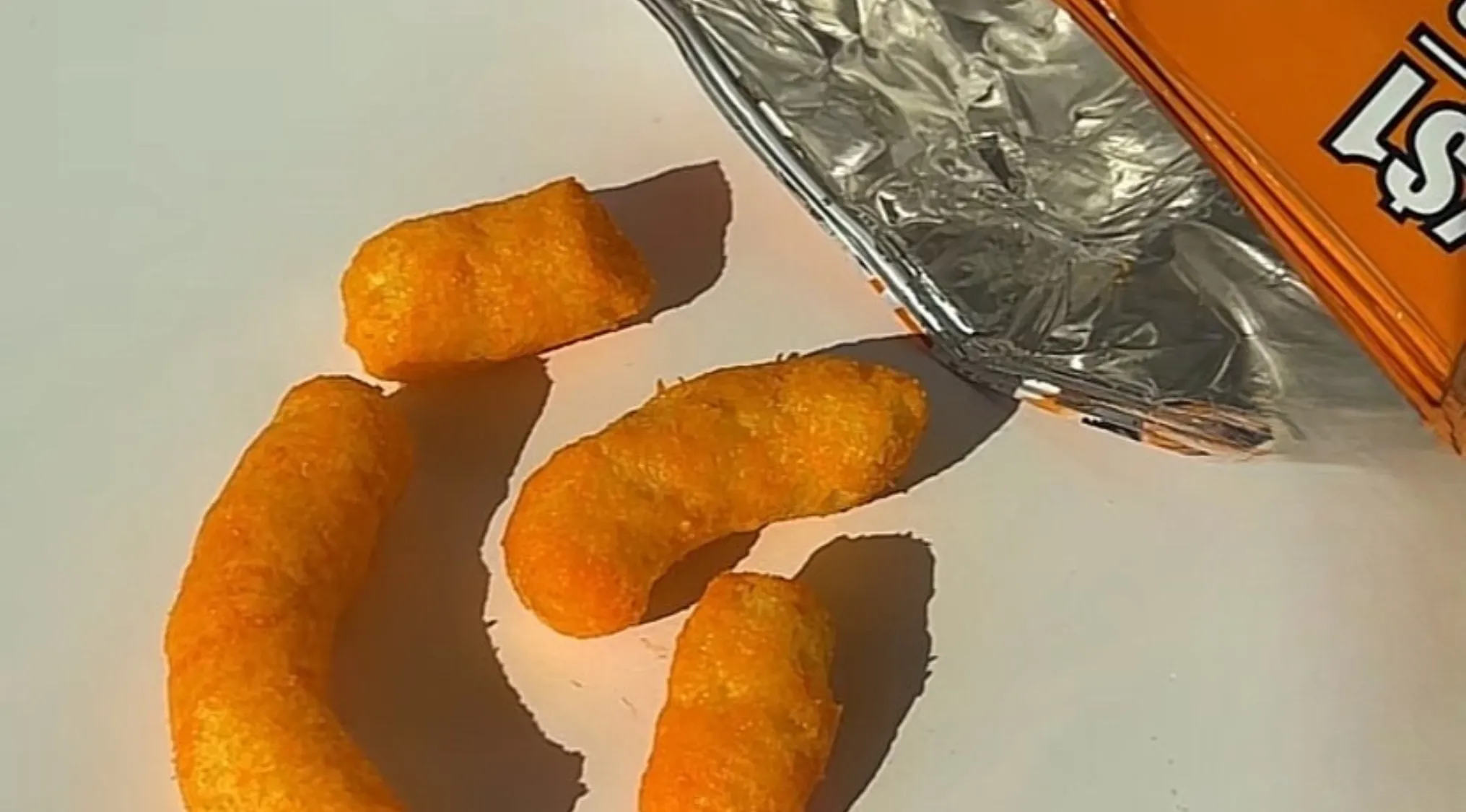 Close-up of orange cheesy chips next to an open foil snack bag, highlighting real chips texture and appearance.