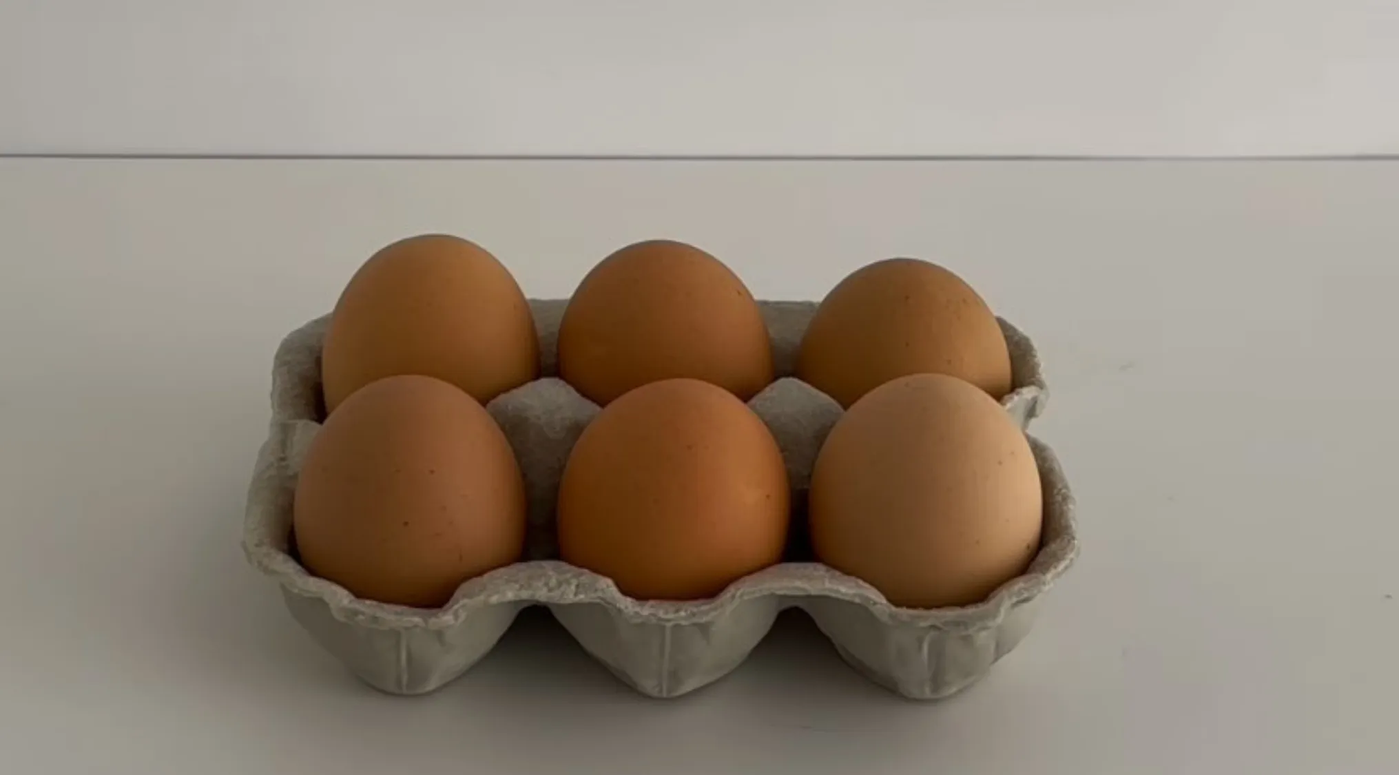 Six brown eggs in a carton on a white surface, questioning if they are real eggs or cake replicas.