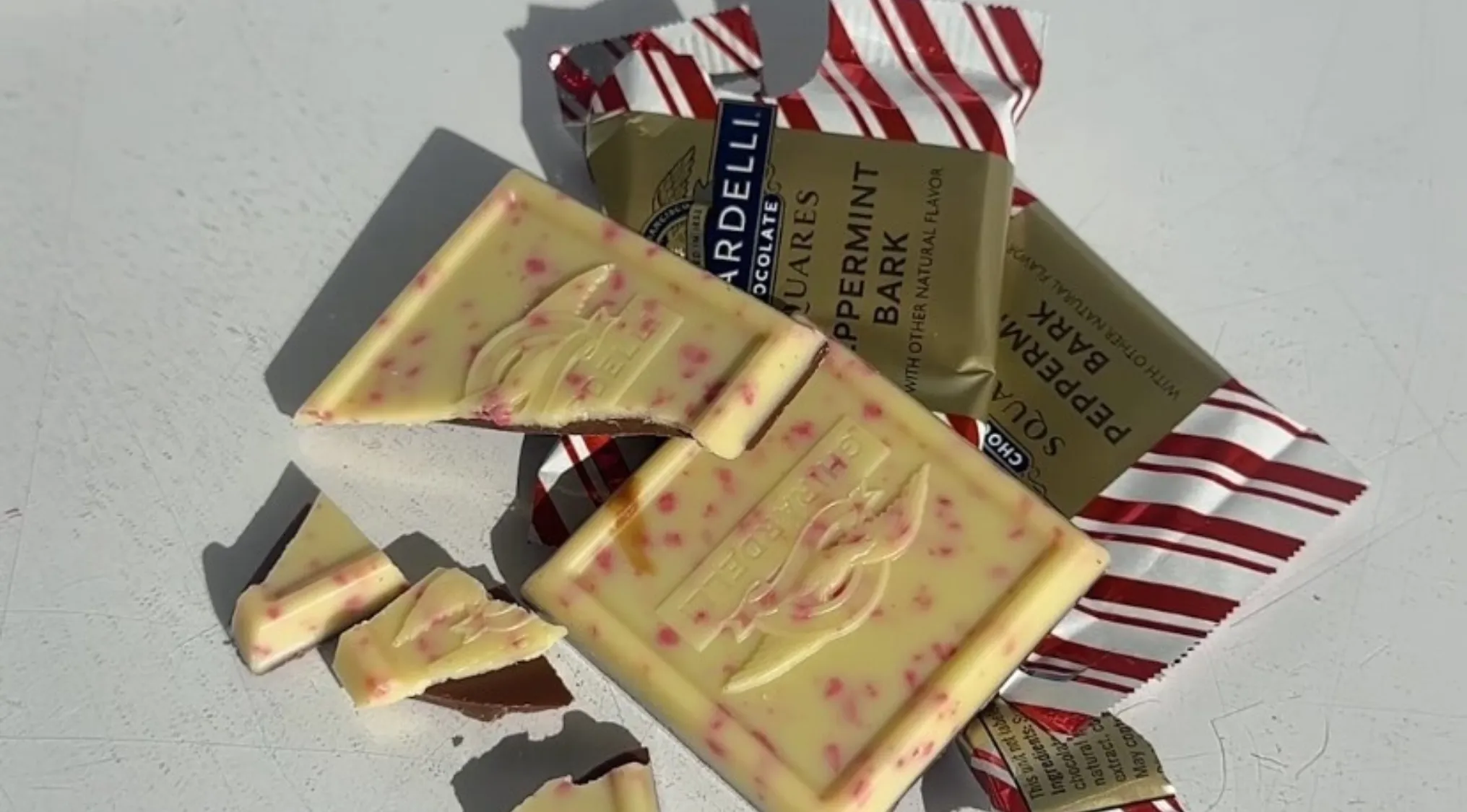 White chocolate peppermint bark broken into pieces with red peppermint bits and packaging on a white surface.