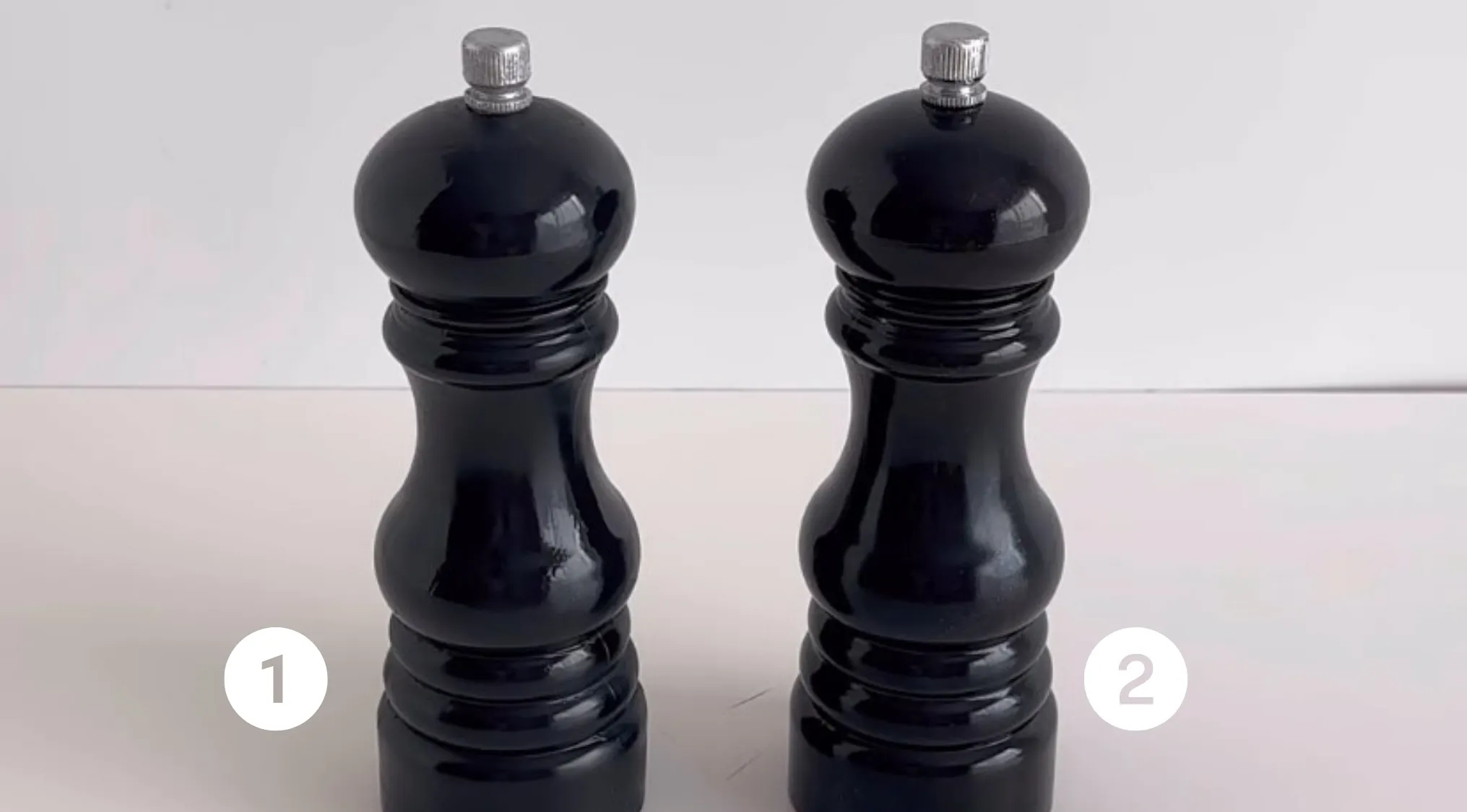Two black pepper grinders on a table in a real or cake challenge with numbers one and two shown.