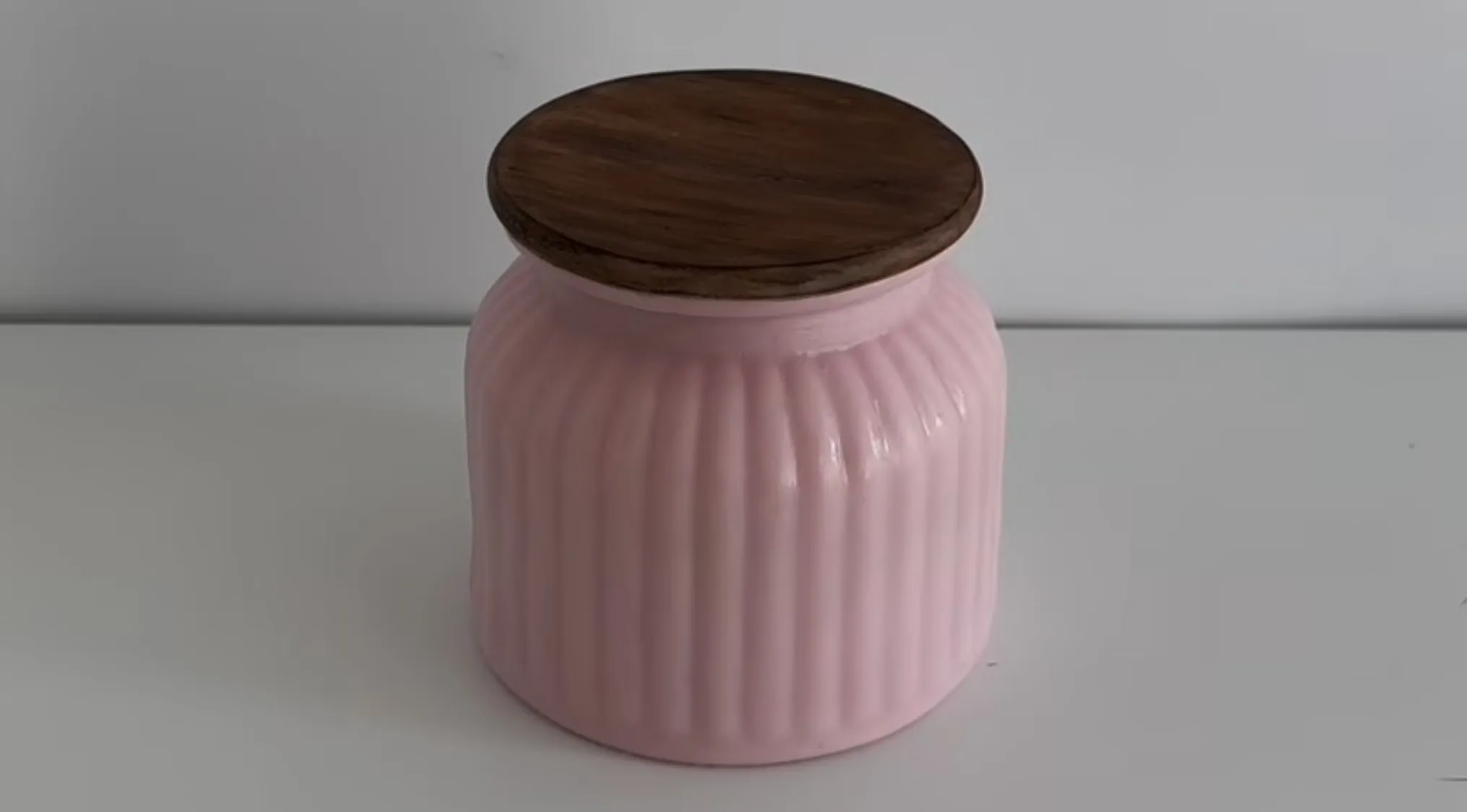 Pink container with wooden lid on a white surface, questioning if it is real, slime, or cake in a close-up view