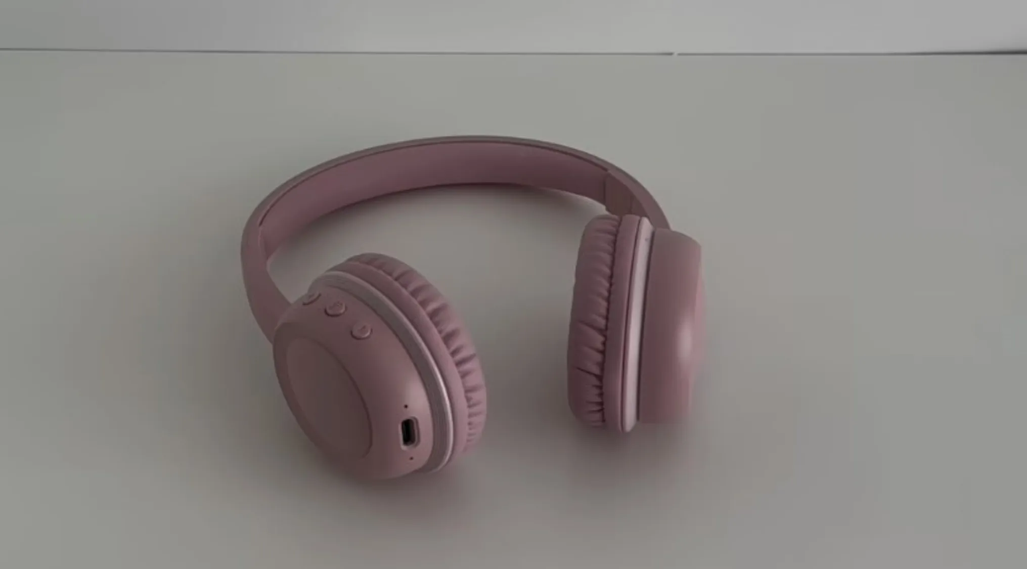 Pink wireless headphones resting on a white surface, raising the question if these headphones are real or cake.