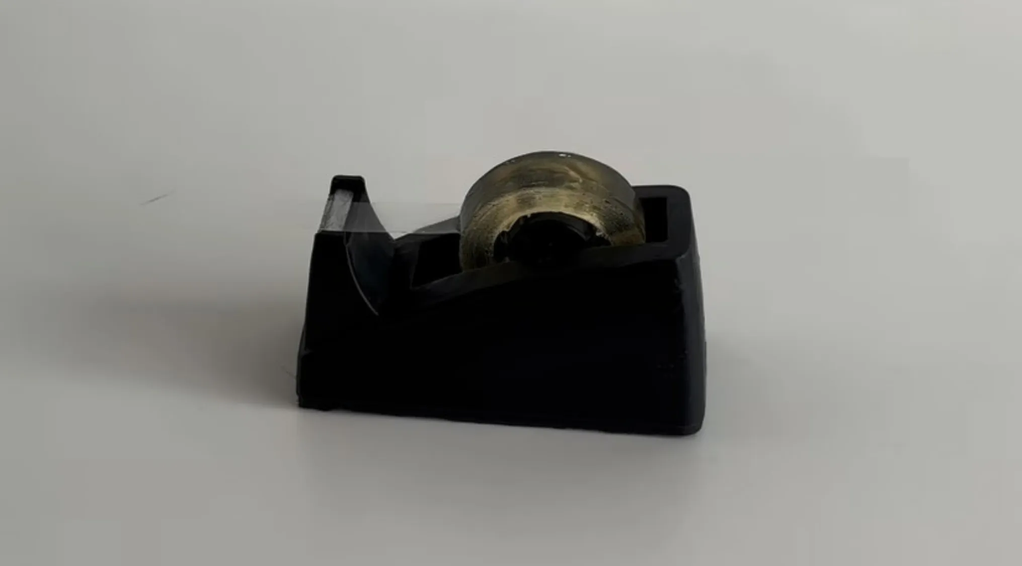 Black sticky tape dispenser with partially used transparent sticky tape on a white surface and blurred background.