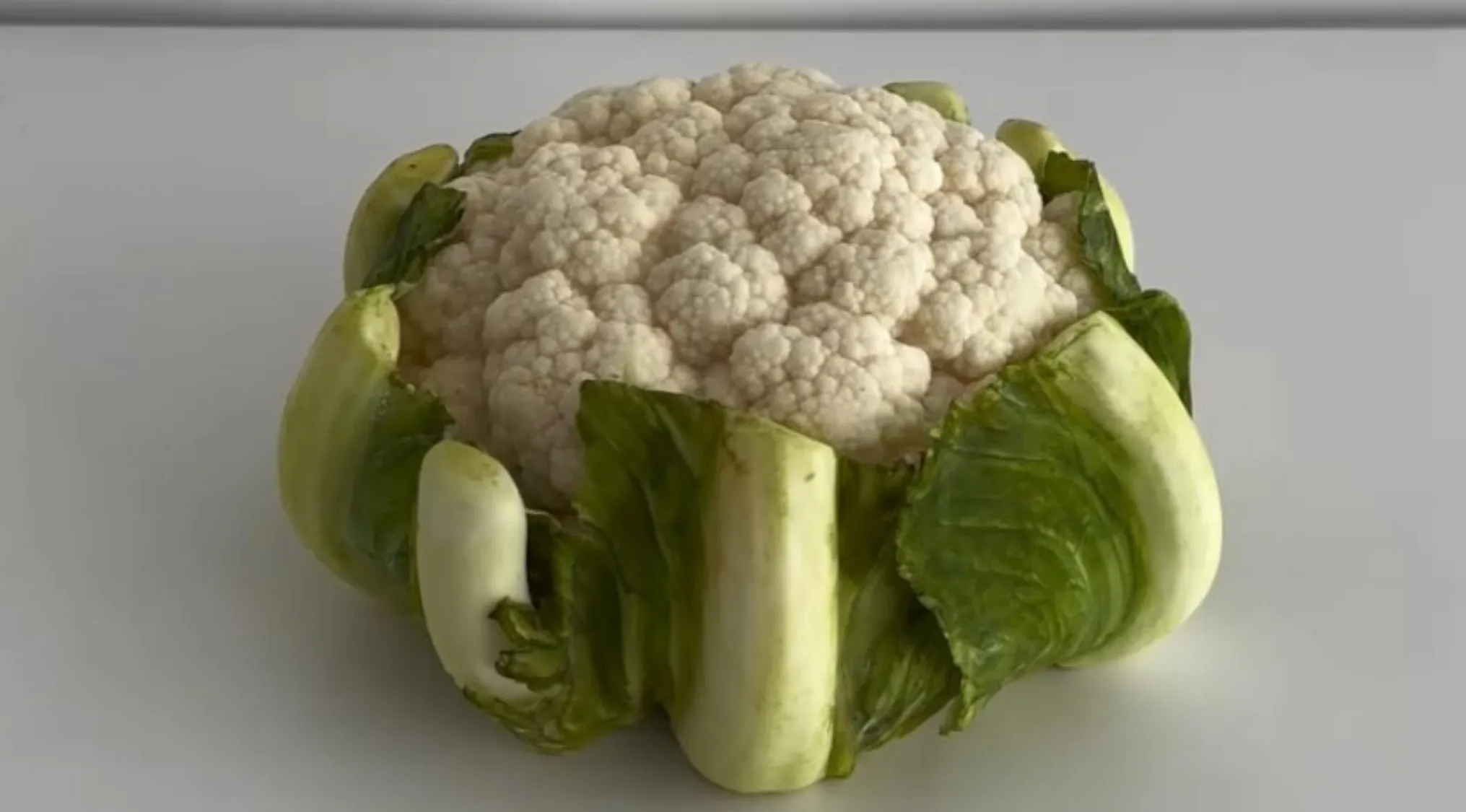 Cauliflower with green leaves on a plain surface, challenging the viewer to guess if it is real or cake.